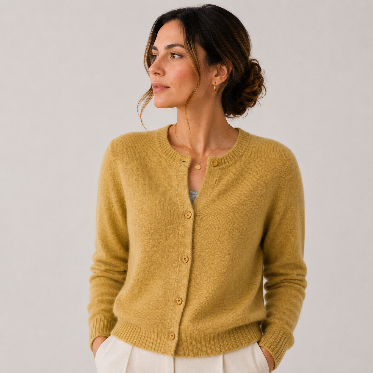A woman wearing a mustard yellow knit cardigan with a button-front closure, shown against a plain light gray studio background.