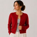 A woman wearing a vibrant red knit cardigan over a gray top and white pants, photographed against a neutral light gray studio background.