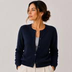 A woman wearing a navy blue knit cardigan over a light gray top and cream pants, photographed against a plain light gray studio background.
