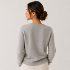 A woman shown from the back wearing a light gray knit sweater and cream pants against a plain light gray studio background.