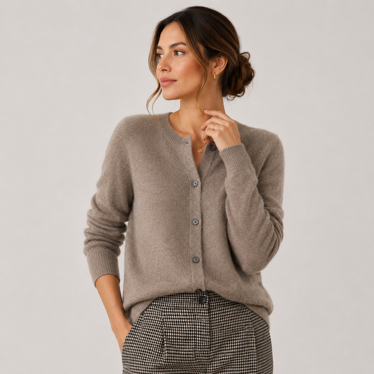 A woman wearing a taupe knit cardigan sweater and a black-and-white houndstooth patterned skirt, posing against a light gray studio background.