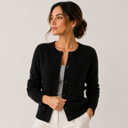 A woman wearing a black button-front cardigan over a light gray top and white pants, photographed against a plain light gray studio background.