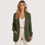 A woman modeling a ribbed olive green open-front cardigan over a cream camisole and cream trousers, photographed against a clean light gray studio background.