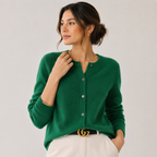 A woman wearing a vibrant green knit cardigan sweater with white pants and a black belt with a gold buckle, posed against a light gray studio background.