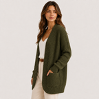 A woman modeling a ribbed knit open-front cardigan in olive green, worn over a white top and cream pants against a plain light background.