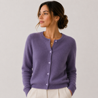 A woman wearing a lavender purple knit cardigan sweater with white buttons, paired with cream-colored pants, photographed against a neutral light gray studio background.