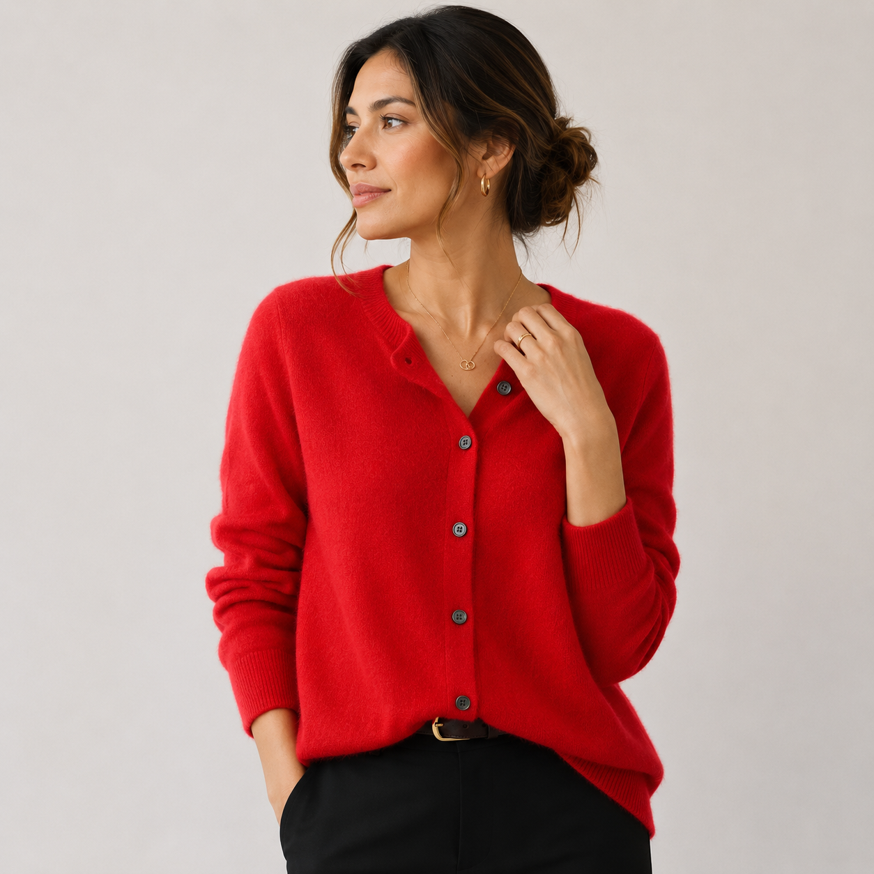 A woman wearing a bright red knit button-front cardigan sweater with a V-neck, paired with black pants, photographed against a plain light gray studio background.