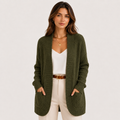 A woman modeling a ribbed open-front cardigan sweater in olive green, worn over a white top and cream pants with a brown belt, against a plain light background.