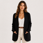 A woman modeling a black ribbed open-front cardigan over a white top and cream pants, photographed against a clean light gray studio background.