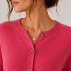 A close-up of a woman wearing a bright pink ribbed knit cardigan with dark buttons and a delicate gold necklace, shown against a light neutral background.