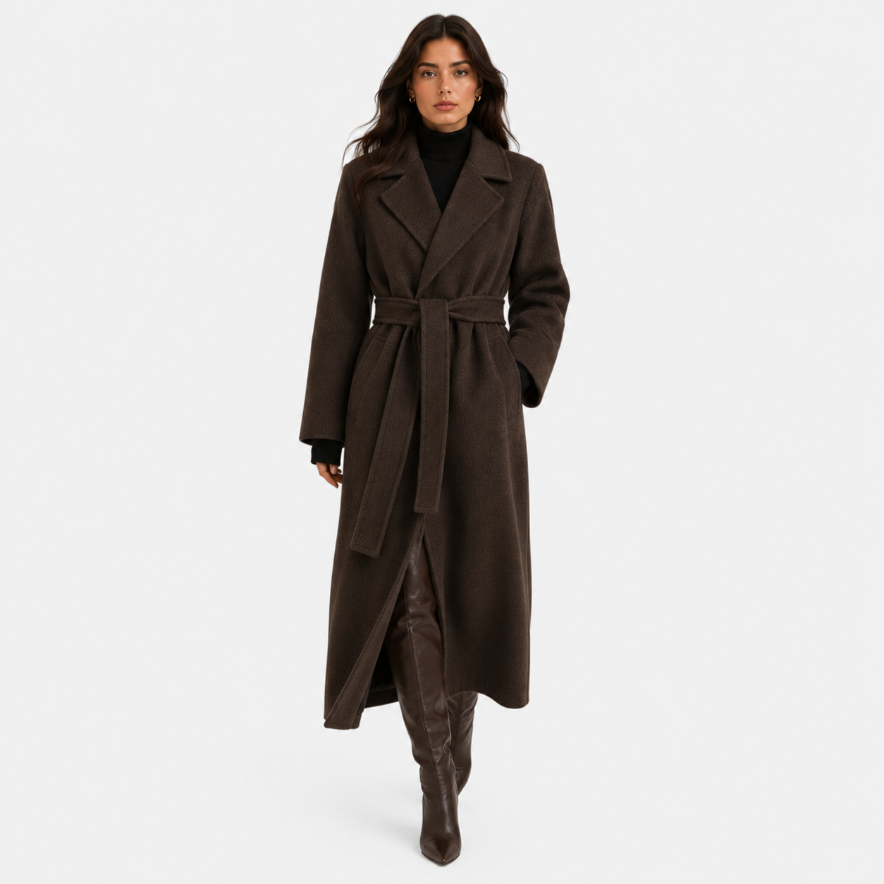 A woman modeling a long dark brown wool-blend coat with a matching waist tie belt, worn over a black turtleneck and brown knee-high boots, against a light gray studio background.