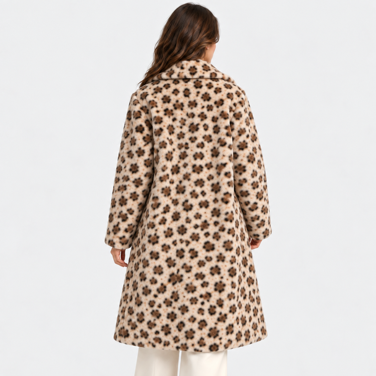 A woman viewed from behind wearing a beige faux-fur coat with a dark brown floral pattern, paired with white pants, against a plain light gray background.