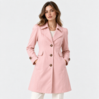 A woman modeling a light pink double-breasted trench coat with dark brown buttons, paired with white pants, against a plain white studio background.