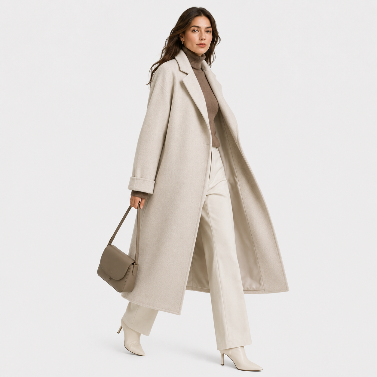 A woman models a long, light beige wool coat over a taupe turtleneck, cream wide-leg trousers, and beige heeled boots, while carrying a taupe leather shoulder bag against a solid light gray background.