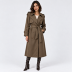 A woman modeling a mid-length olive brown trench coat with a tie waist belt, double-breasted buttons, and shoulder epaulets, paired with dark brown heeled boots against a light gray studio background.
