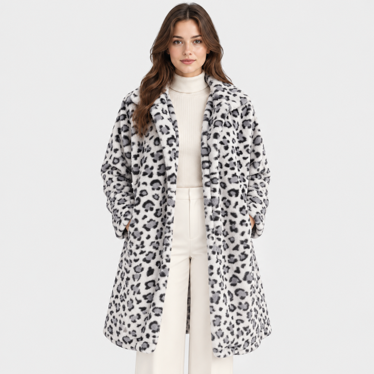A woman modeling a long white faux-fur coat with a black leopard print pattern, worn over a cream turtleneck and cream pants, against a light gray studio background.