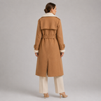 A woman shown from the back wearing a camel-colored trench coat with a cream shearling-style collar and cuffs, paired with cream wide-leg pants and beige heels, against a neutral gray studio background.
