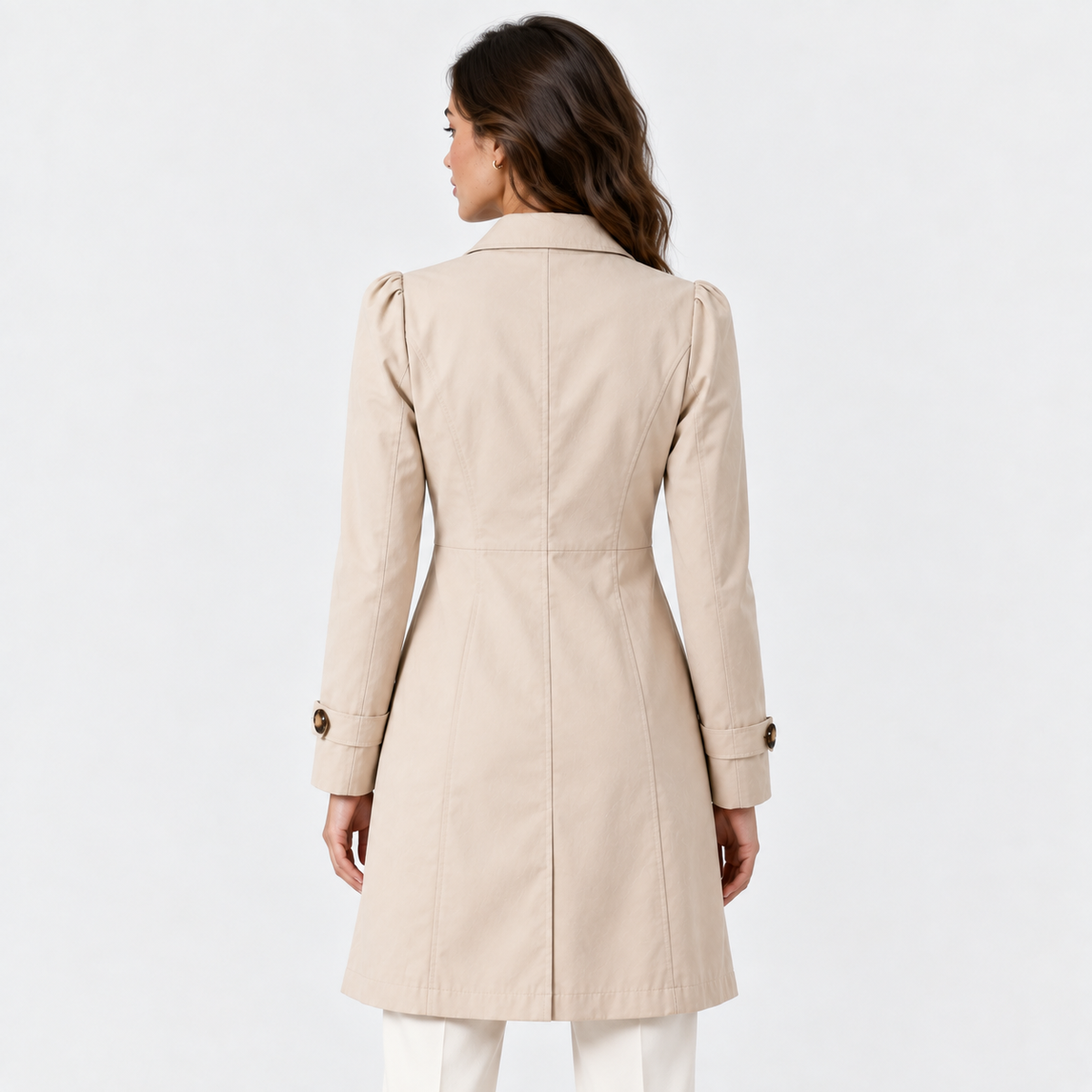 A woman shown from the back wearing a light beige trench coat with puffed sleeves and white pants, photographed against a clean white studio background.