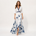 A woman models a white maxi dress with a blue watercolor floral print and navy trim, standing against a plain white studio background.