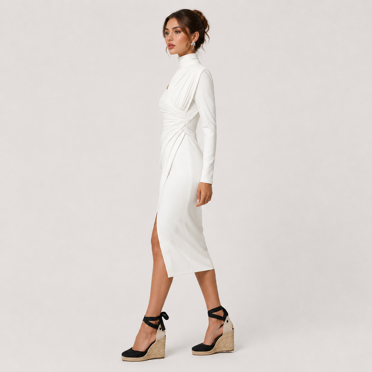 A woman modeling a white long-sleeve midi dress with a high mock neck, gathered waist, and side slit, paired with black wedge sandals, against a light gray studio background.