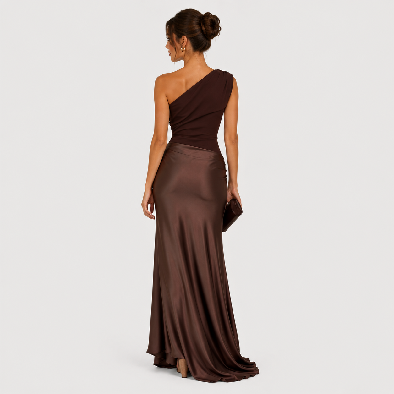 A woman wearing a floor-length one-shoulder satin gown in dark brown, shown from the back against a light gray studio background.