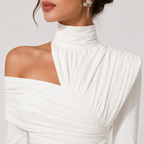A close-up of a model wearing a white off-the-shoulder long-sleeve dress with a high gathered mock neck and pleated draping details.