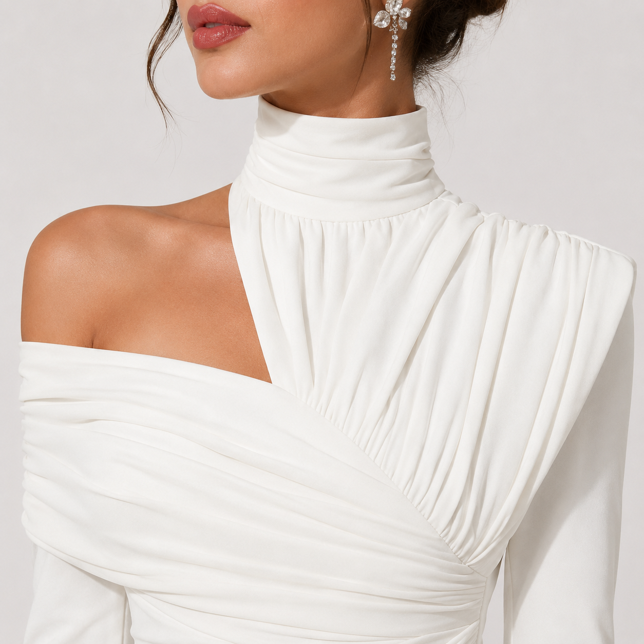 A close-up of a model wearing a white off-the-shoulder long-sleeve dress with a high gathered mock neck and pleated draping details.