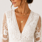 A close-up of a woman wearing a white lace and mesh deep V-neck top with floral embroidery on the sleeves, styled with layered gold necklaces.