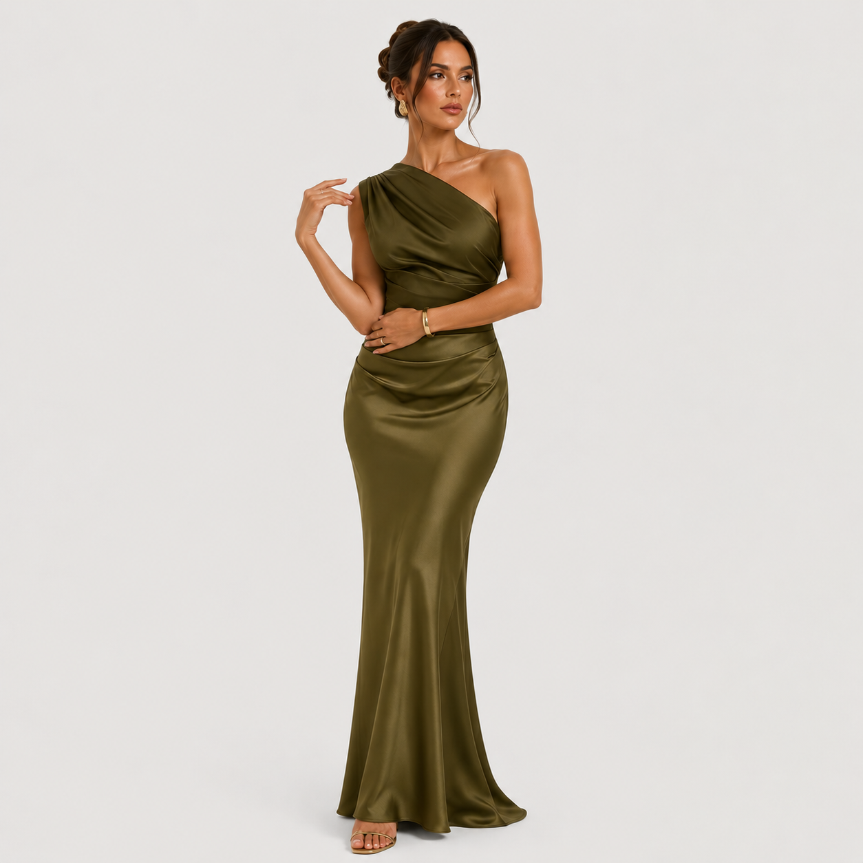 A woman models a floor-length, one-shoulder satin gown in olive green against a plain light gray studio background.