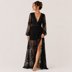 A woman models a black lace maxi dress with sheer long sleeves, a deep V-neckline, and a high thigh slit, set against a plain light gray studio background.