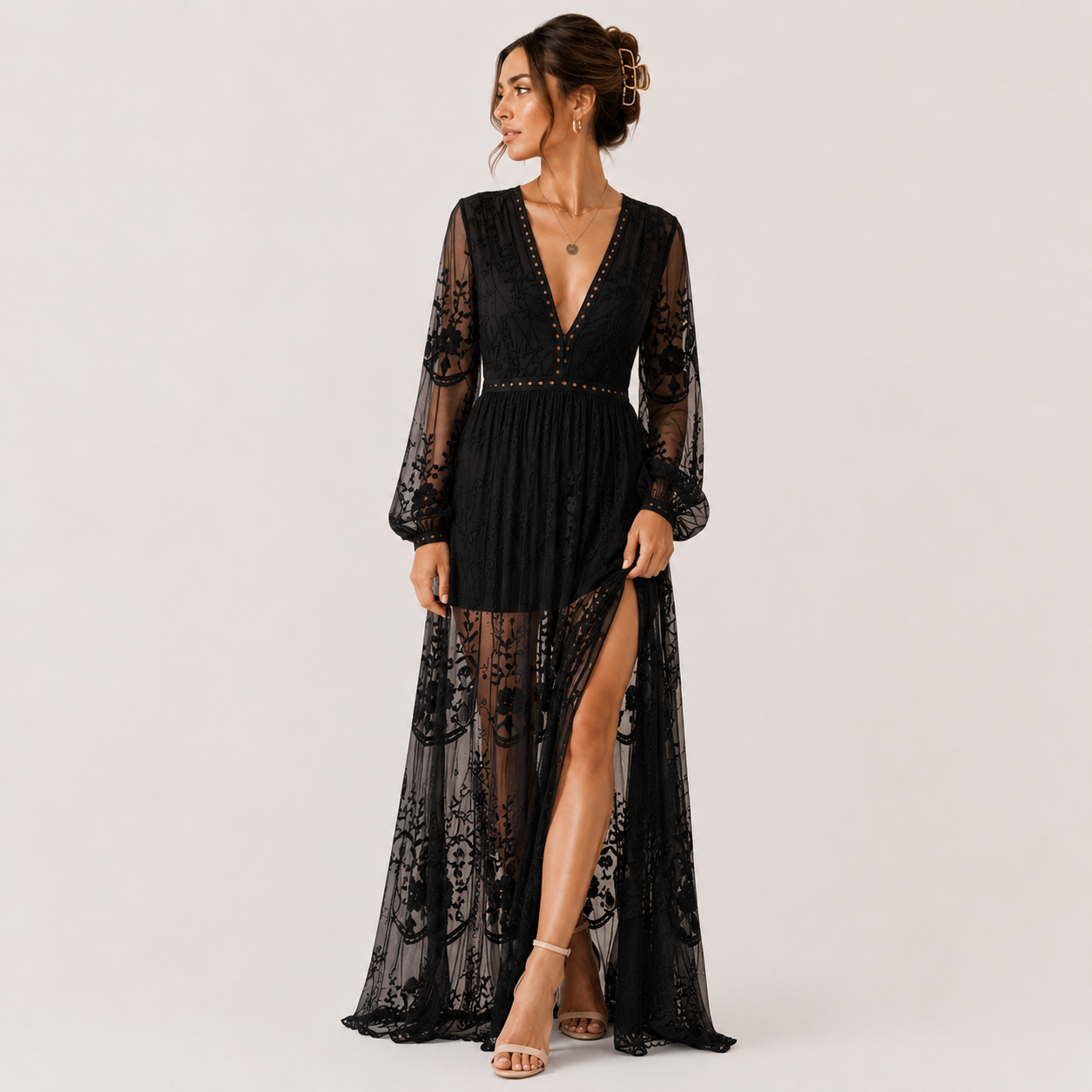 A woman models a black lace maxi dress with sheer long sleeves, a deep V-neckline, and a high thigh slit, set against a plain light gray studio background.