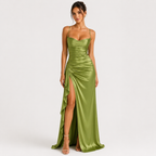A woman modeling a floor-length olive green satin gown with spaghetti straps, a sweetheart neckline, ruched detailing, and a high thigh slit, photographed against a plain light gray studio background.