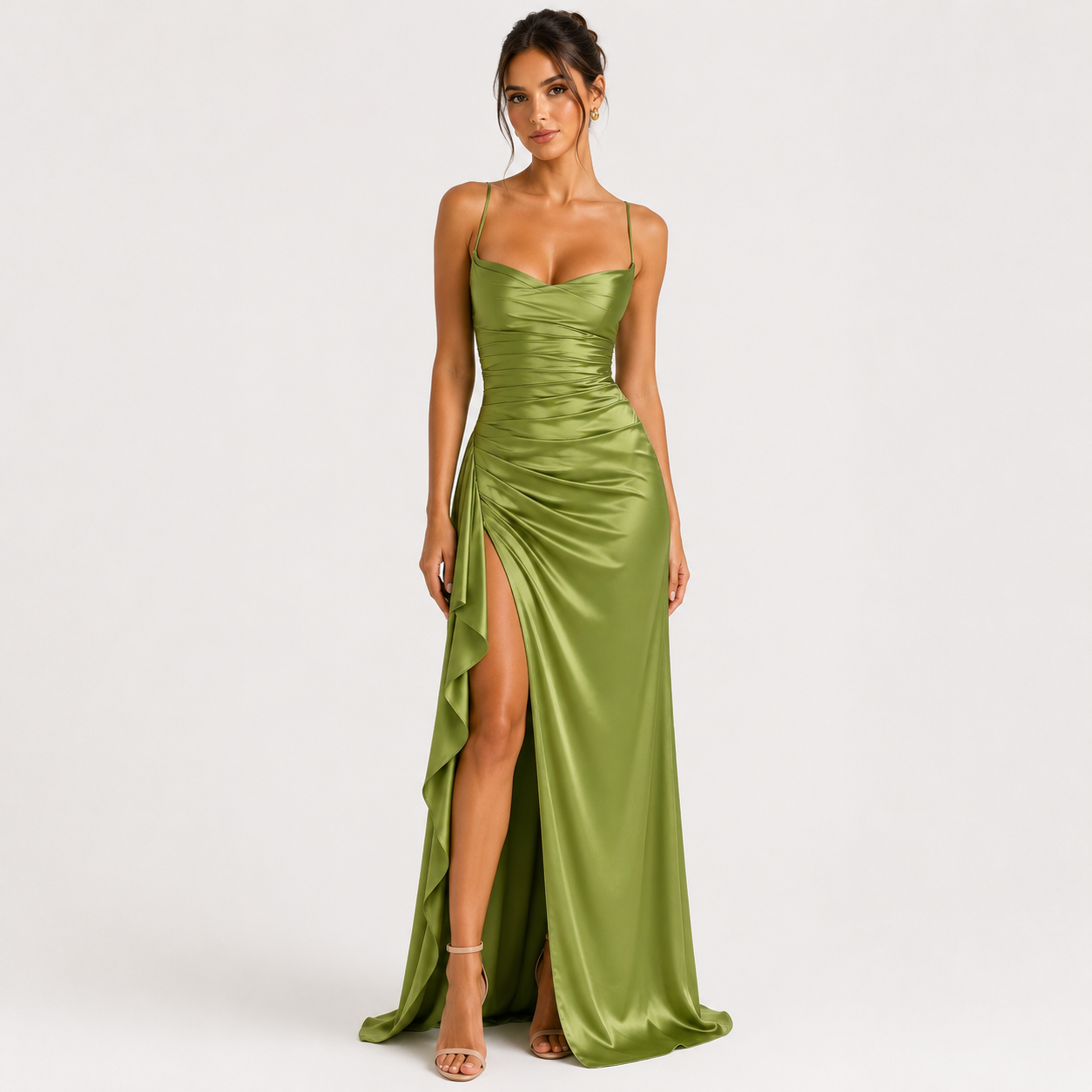 A woman modeling a floor-length olive green satin gown with spaghetti straps, a sweetheart neckline, ruched detailing, and a high thigh slit, photographed against a plain light gray studio background.