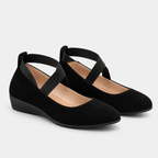 A pair of black suede Mary Jane flats with adjustable ankle straps and a low wedge heel, shown on a light gray background.