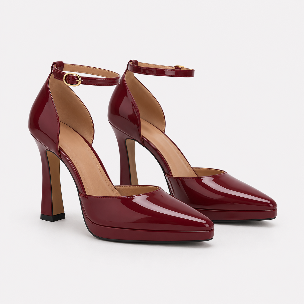 A pair of glossy burgundy patent leather high-heeled pumps with ankle straps and gold-tone buckle details, displayed on a clean light gray background.