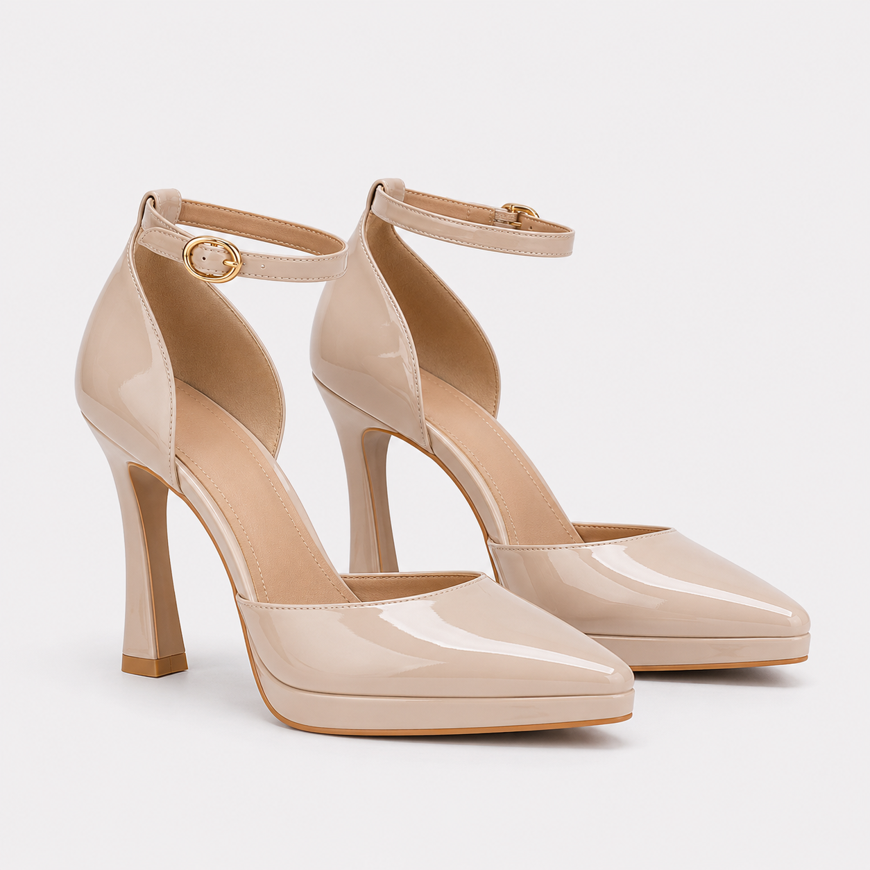 A pair of beige patent leather high-heeled pumps with ankle straps and gold-tone hardware, shown on a light gray background.