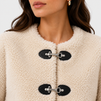 Close-up of a person wearing a cream sherpa fleece coat with black toggle closures and silver metal hardware.