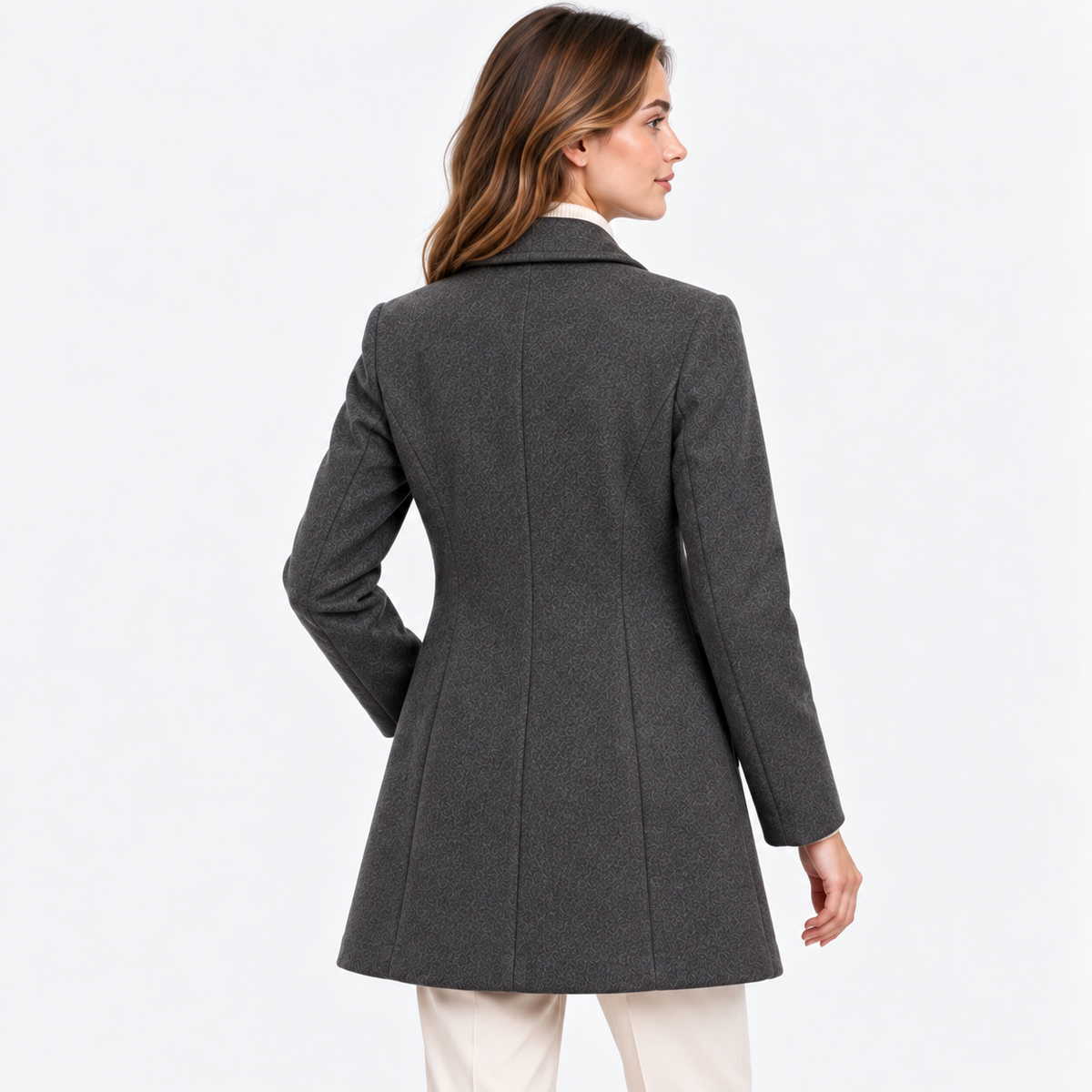 A woman shown from the back wearing a dark gray structured blazer or coat over a white collared shirt and light beige pants, photographed against a clean white studio background.