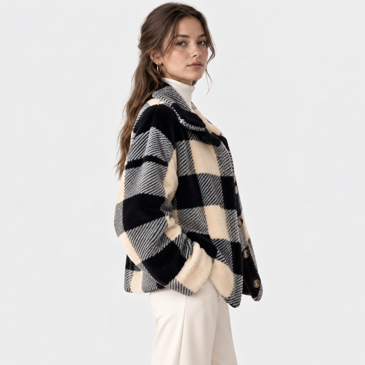 A woman wearing a black and cream buffalo check plaid fuzzy cardigan over a white mock neck top and cream pants, photographed against a clean white studio background.
