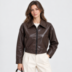 A woman modeling a dark brown faux-leather cropped jacket with a front zipper, collar, and elasticized hem, paired with cream pants against a light gray studio background.