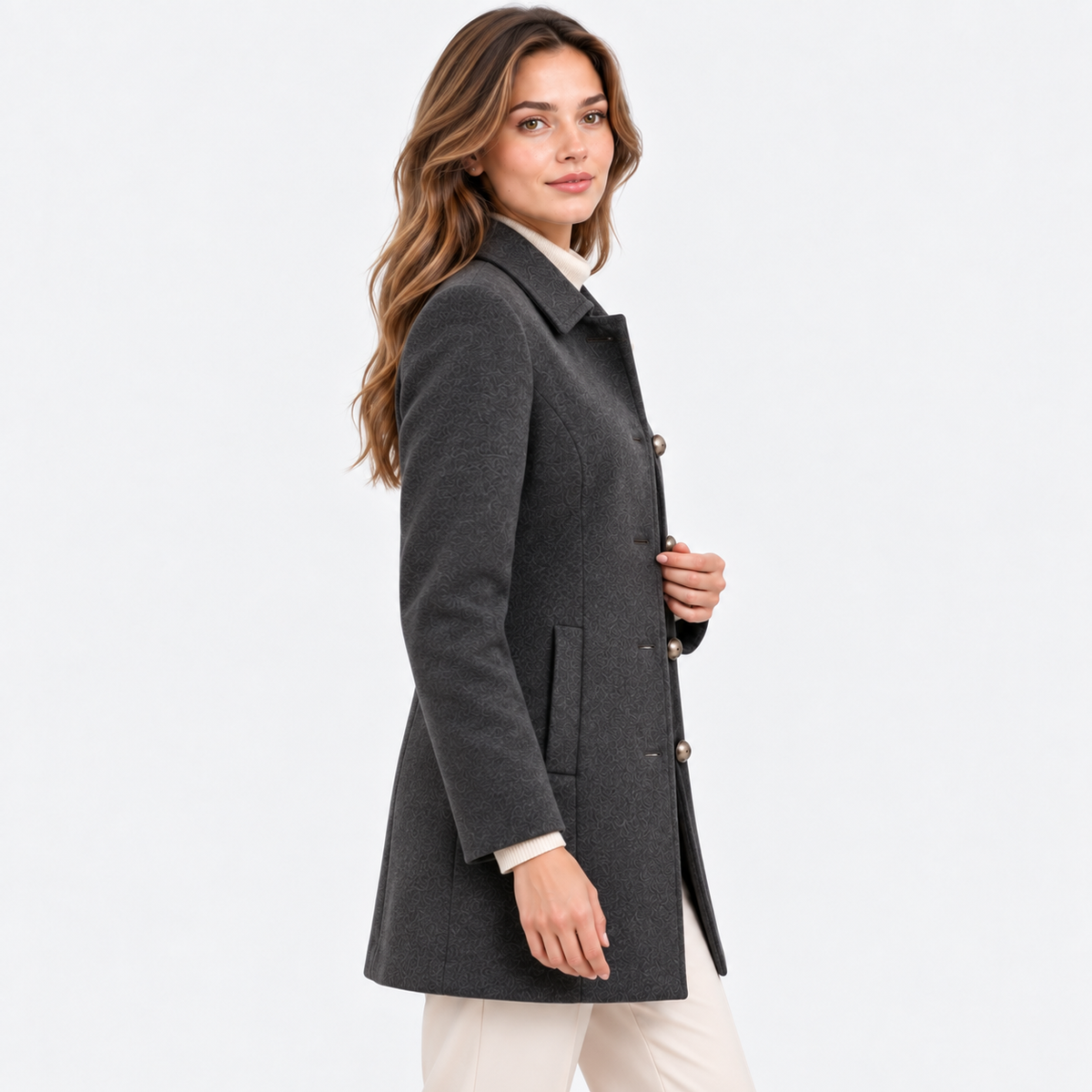 A woman modeling a dark gray wool-blend coat with brown buttons, worn over a cream collared shirt and cream trousers, against a plain white studio background.