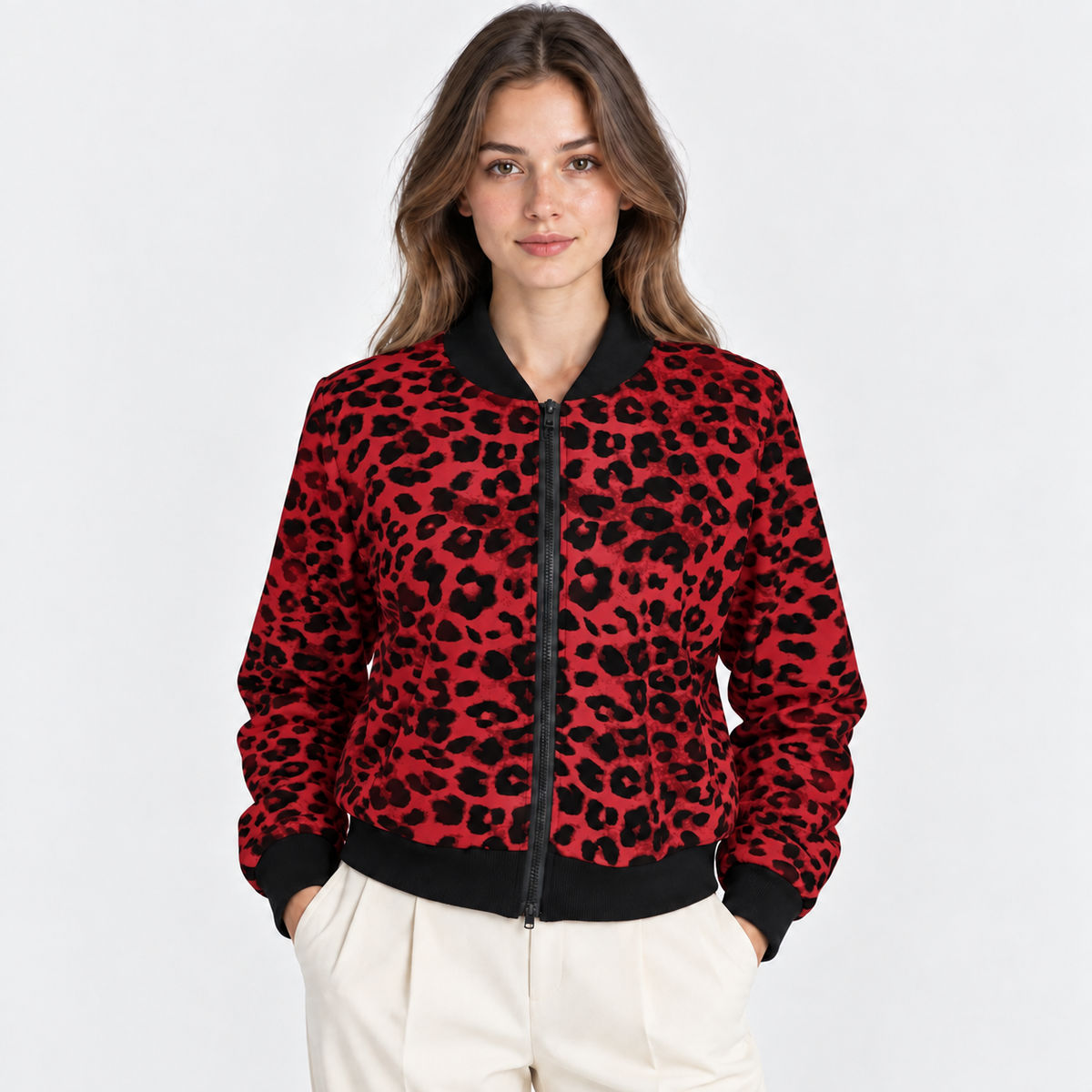 A woman modeling a red and black leopard-print bomber jacket with black ribbed trim, paired with cream pants, against a plain light gray background.