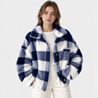 A woman wearing a navy and white checkered fuzzy teddy jacket over a white top and white pants, photographed against a light gray studio background.