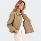 Side angle of a woman wearing a beige button-front jacket with white pants