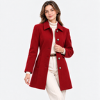 A woman modeling a red knee-length coat over a cream turtleneck and cream pants, photographed against a clean light gray studio background.