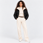 Woman wearing a black quilted puffer jacket with cream shearling collar and white pants