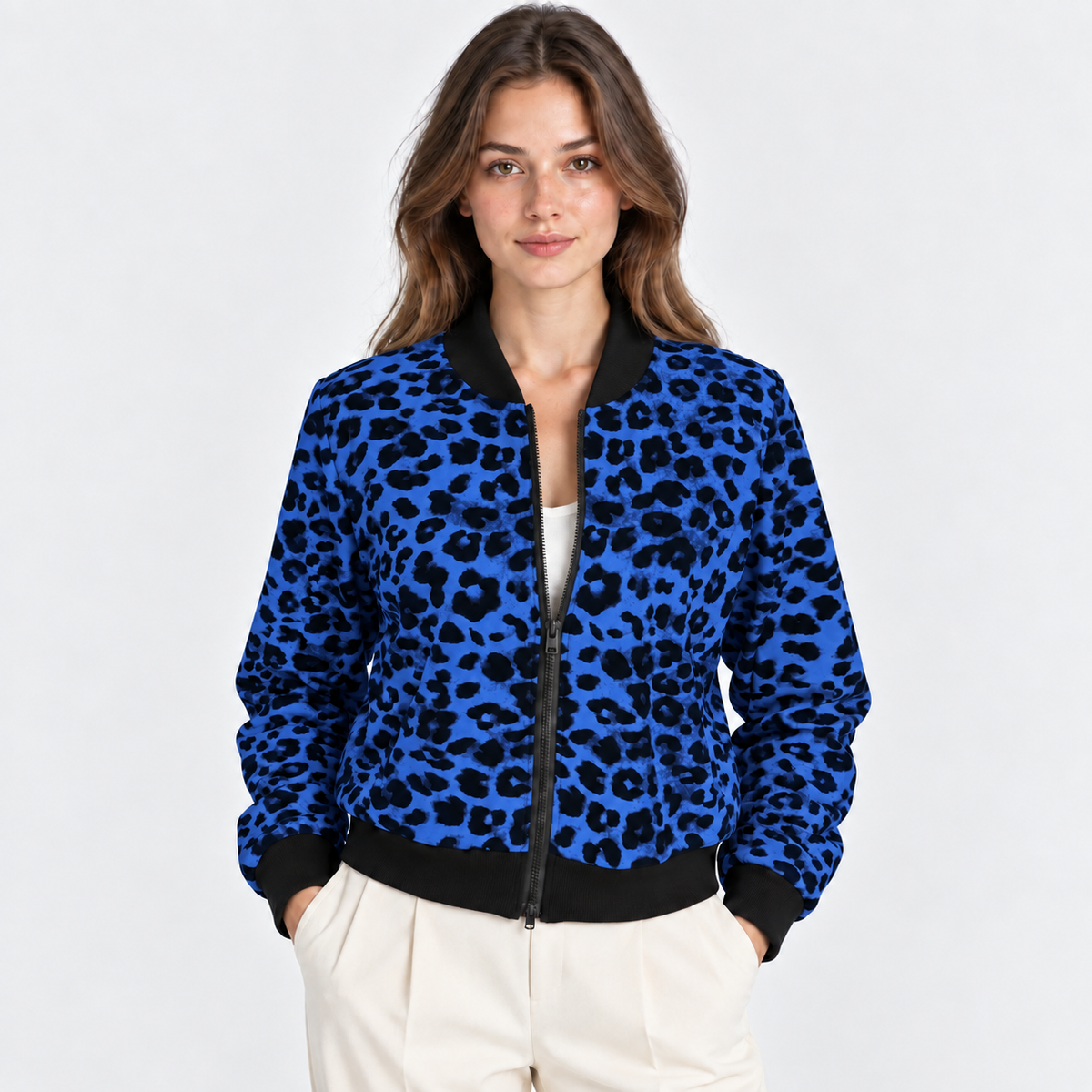 A woman modeling a blue and black leopard-print bomber jacket with black ribbed collar, cuffs, and hem, paired with cream trousers, against a light gray studio background.