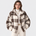 A woman modeling a brown and cream buffalo plaid fuzzy faux fur cardigan jacket, styled with a cream ribbed turtleneck, cream pants, and gold jewelry against a light gray studio background.