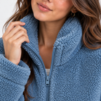 Close-up of a woman wearing a dusty blue sherpa fleece zip-up jacket, showing the textured fabric and collar.