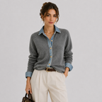 A woman models a gray knit cardigan layered over a light blue denim button-up shirt, paired with cream trousers and a brown belt, against a plain light gray studio background.